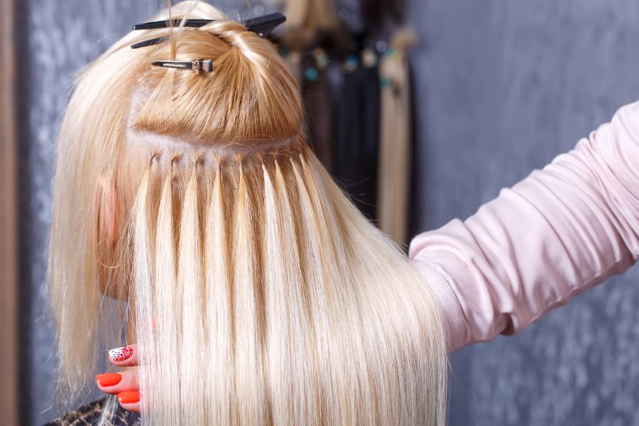 Hairdresser doing hair extensions for young girl in salon